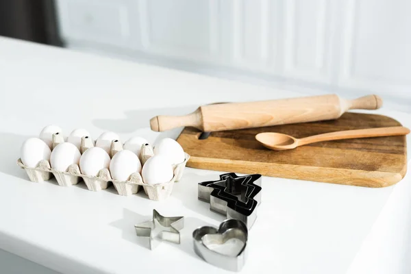 Ovos, tábua de corte, colher, moldes de massa e rolo de pino na mesa — Fotografia de Stock