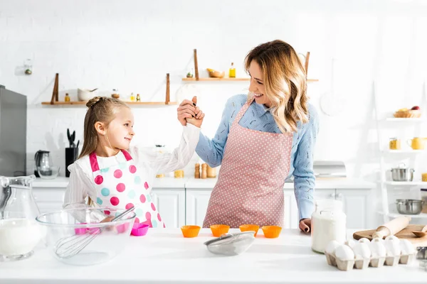 Sonriente madre cogida de la mano con linda hija en la cocina - foto de stock