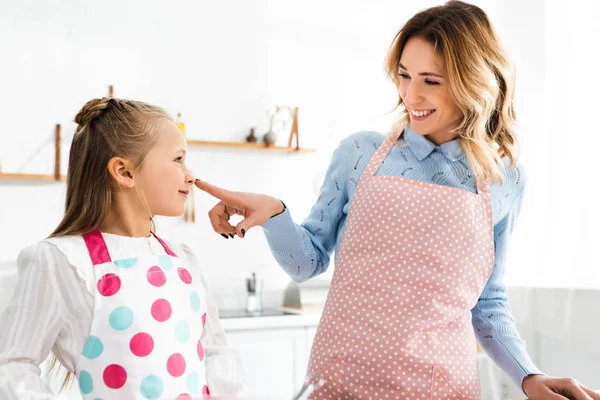 Sonriente madre tocando la nariz de su linda hija en la cocina - foto de stock