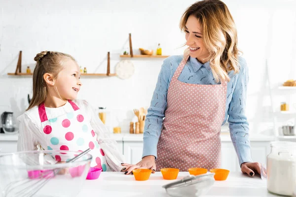 Sorrindo mãe e filha em aventais olhando um para o outro — Fotografia de Stock