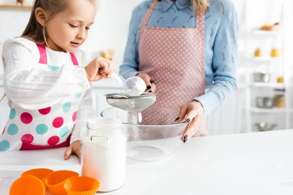 Abgeschnittene Ansicht der Mutter mit Sieb und der niedlichen Tochter, die Mehl siebte — Stockfoto