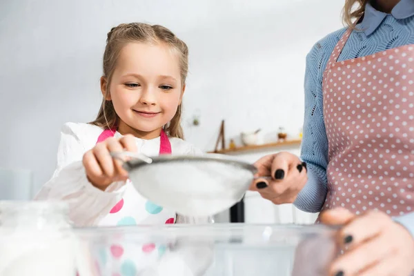 Abgeschnittene Ansicht der Mutter mit Sieb und lächelnder Tochter, die Mehl siebte — Stockfoto