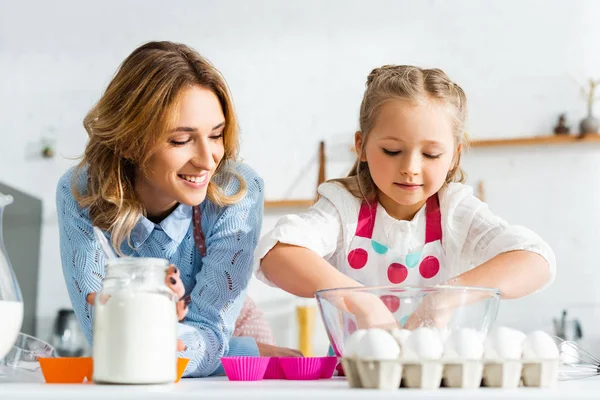 Sonriente madre mirando hija cocinar masa para pastelería - foto de stock