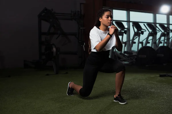 Giovane donna afroamericana adulta stringendo le mani e facendo affondi in palestra — Foto stock