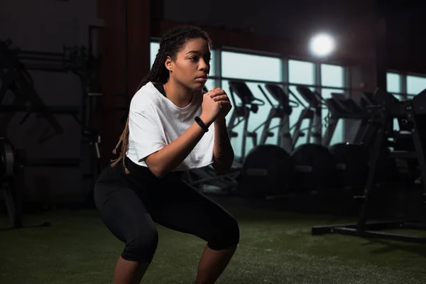African american woman clenching hands and squating in gym — Stock Photo