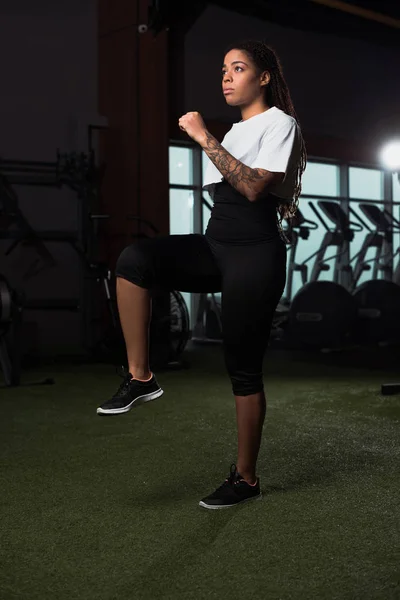 Afroamerikanerin hebt Bein und Hand beim Aufwärmen im Fitnessstudio — Stockfoto