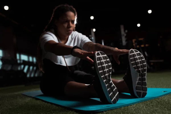 Selective focus of african american woman sitting and stretching on fitness mat — Stock Photo