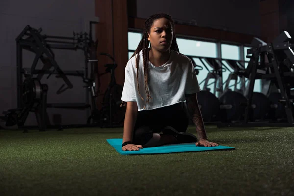 Mujer afroamericana sentada en postura de yoga en colchoneta de fitness - foto de stock