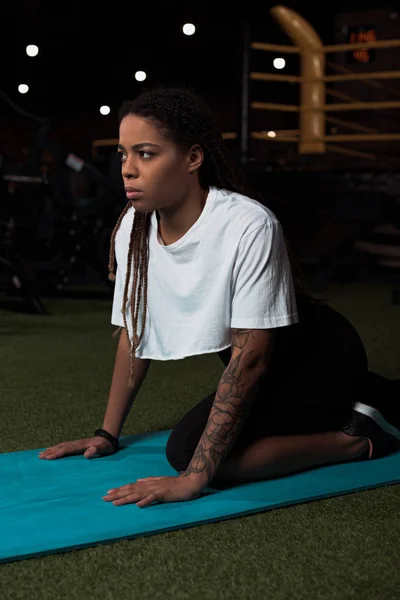 African american woman sitting on fitness mat in gym — Stock Photo