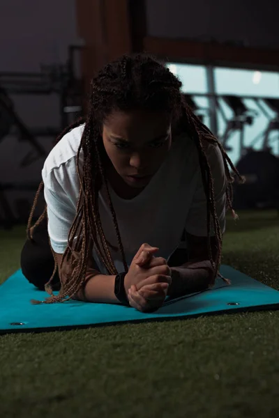 Femme afro-américaine stressée et mécontente assise les mains serrées sur un tapis de fitness — Photo de stock