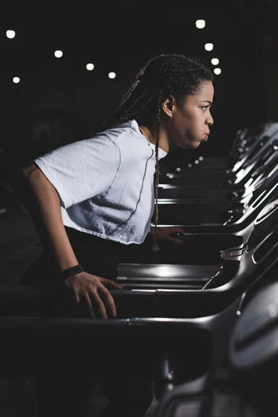 Seitenansicht einer Afroamerikanerin, die beim Laufen auf dem Laufband die Wangen ausbläst — Stockfoto