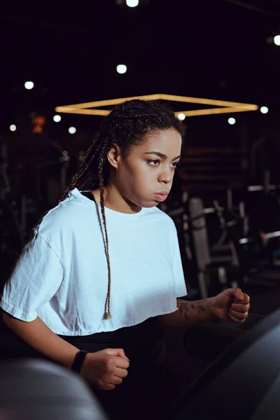 Selective focus of african american woman puffing out cheeks while running on treadmill — Stock Photo