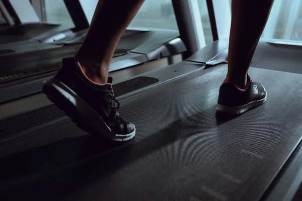 Vista recortada de las piernas de mujer afroamericana con zapatillas en la cinta de correr en el gimnasio - foto de stock