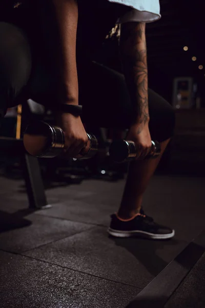 Vue recadrée de femme afro-américaine accroupie avec haltères dans la salle de gym — Photo de stock