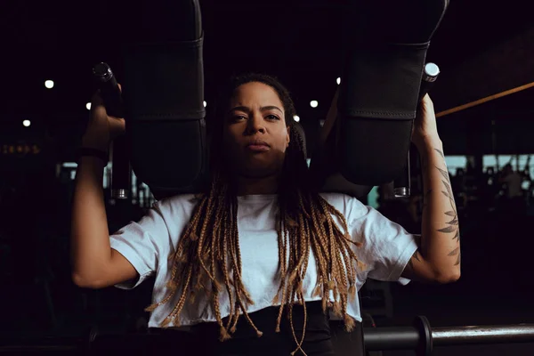 Mujer afroamericana tatuada haciendo ejercicio en la máquina de fitness — Stock Photo