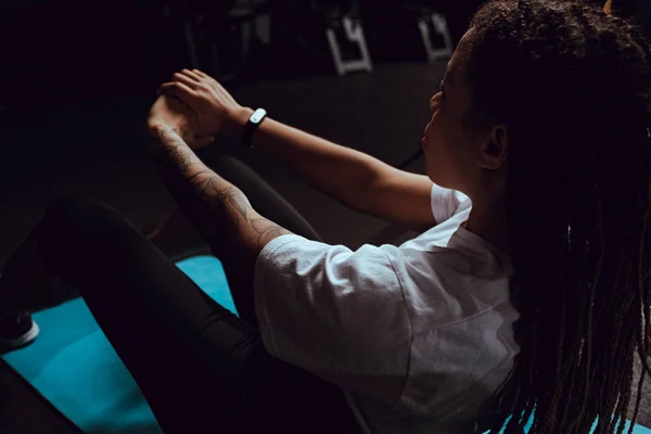 Selective focus of tattooed african american woman with dreadlocks doing exercise in gym — Stock Photo