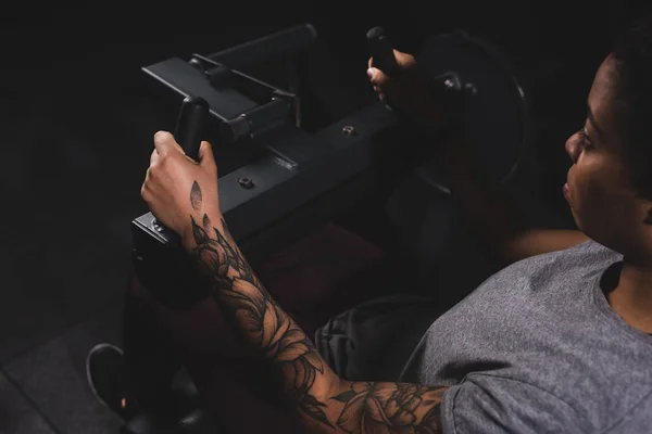 Enfoque selectivo de la mujer afroamericana tatuada que hace ejercicio en la máquina de fitness - foto de stock