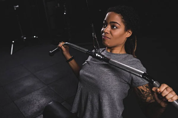 Joven afroamericano chica con tatuaje entrenamiento en gimnasio máquina - foto de stock