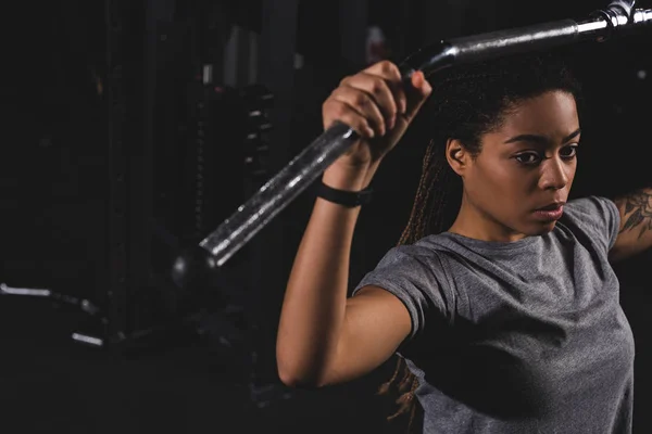 Selective focus of young african american girl with tattoo training on gym machine — Stock Photo