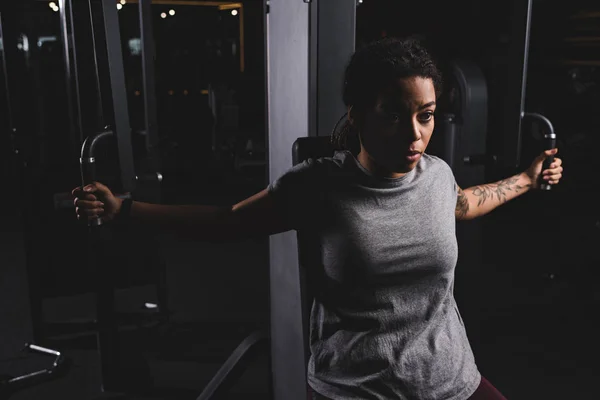 Joven afroamericano chica con tatuaje entrenamiento en gimnasio máquina - foto de stock