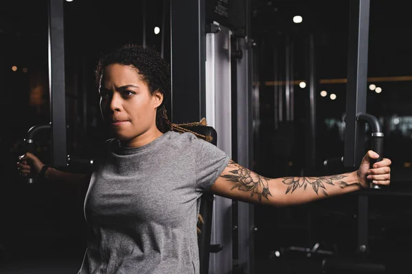 Atractiva chica afroamericana con entrenamiento de tatuaje en la máquina de gimnasio - foto de stock