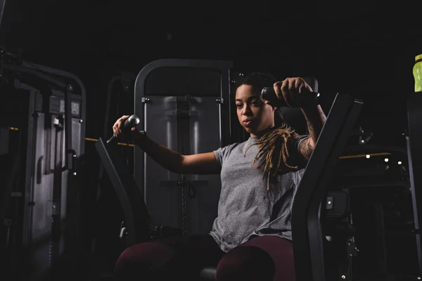 Athlétique et tatoué afro-américaine fille exerçant sur la machine de gymnase — Photo de stock