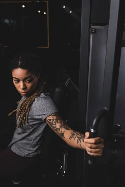 Foyer sélectif de femme africaine américaine sportive et tatouée faisant de l'exercice sur une machine de gymnastique — Photo de stock