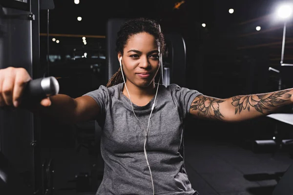 Foyer sélectif de femme afro-américaine heureuse et tatouée écouter de la musique dans la salle de gym — Photo de stock