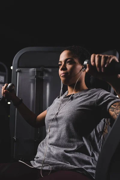 Selective focus of tattooed african american woman listening music while exercising in gym — Stock Photo