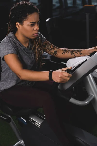 Focused african american girl with tattoo training on gym machine — Stock Photo