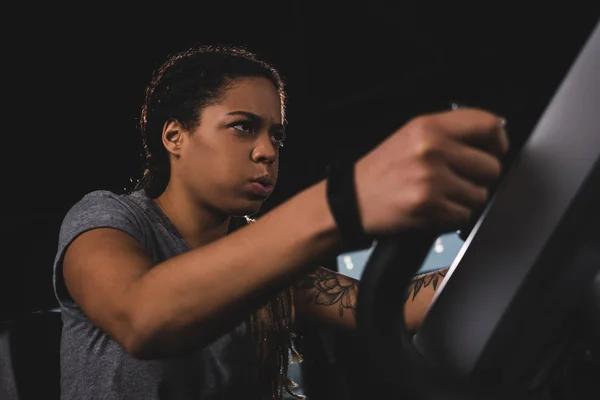 Selective focus of focused african american girl with smartwatch training on gym machine — Stock Photo