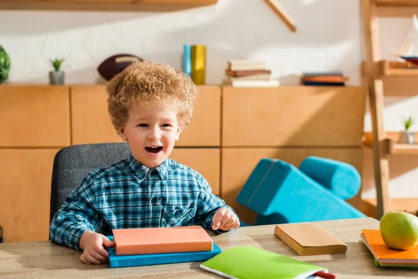 Feliz chico inteligente sonriendo cerca de libros y manzana - foto de stock