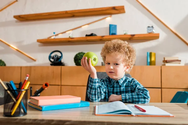 Lindo niño inteligente sosteniendo manzana madura y mirando a la cámara - foto de stock