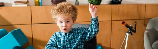 Panoramic shot of emotional smart kid with raised hand at home — Stock Photo