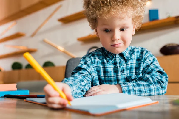 Селективное внимание кудрявого и умного ребенка, пишущего в блокноте — стоковое фото