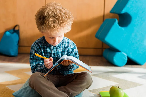 Niño inteligente mirando el cuaderno y la pluma - foto de stock