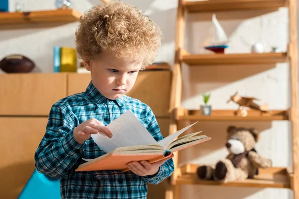 Недовольный и умный ребенок держит книгу дома — стоковое фото