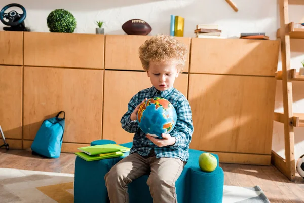 Enfant intelligent tenant globe tout en étant assis près des livres et de la pomme — Photo de stock