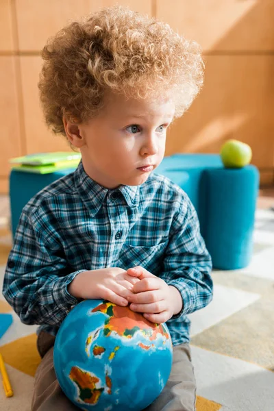 Bambino riccio e intelligente che tiene il globo e distoglie lo sguardo — Foto stock