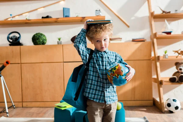 Inteligente y rizado niño con mochila celebración globo y libro por encima de la cabeza - foto de stock