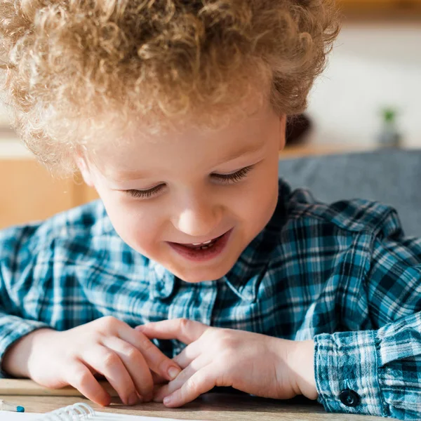 Enfant joyeux souriant tout en regardant la table en bois — Photo de stock