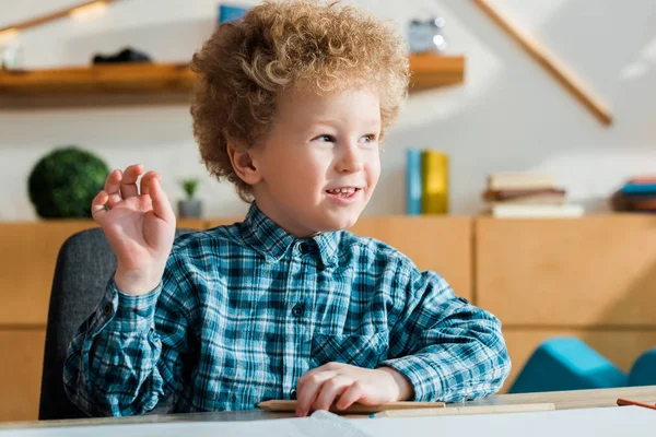 Chico inteligente y rizado con la mano levantada mirando hacia otro lado - foto de stock
