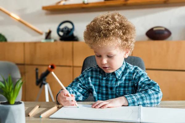 Selective focus of smart and curly kid holding pencil while drawing on blank paper — Stock Photo