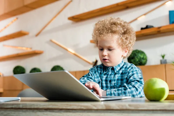 Nettes Kind benutzt Laptop in der Nähe von Apfel zu Hause — Stockfoto