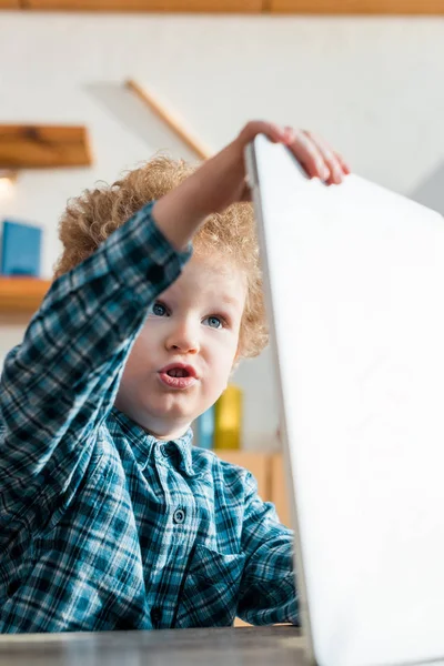 Enfoque selectivo de niño inteligente y rizado mirando el ordenador portátil - foto de stock