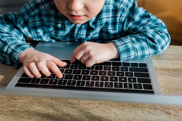 Обрезанный вид симпатичного мальчика, печатающего на клавиатуре ноутбука — стоковое фото