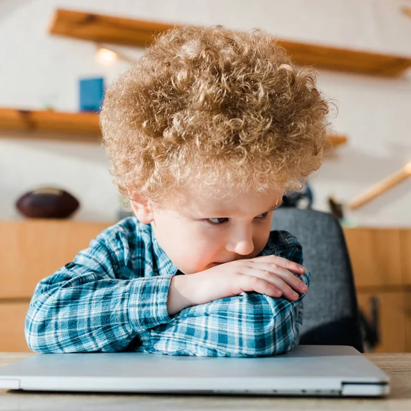 Niño pensativo e inteligente sentado cerca de la computadora portátil - foto de stock