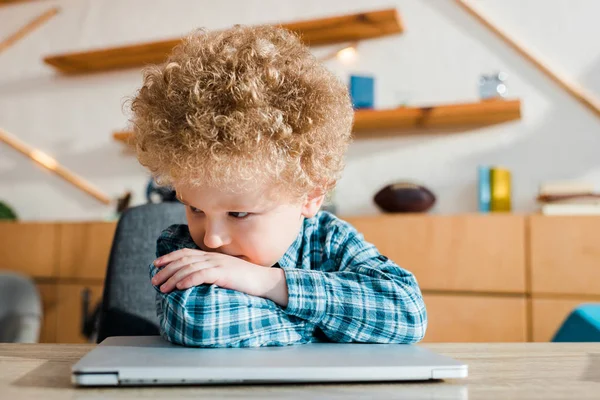 Bambino pensieroso e intelligente che guarda lontano vicino al computer portatile — Foto stock