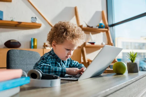 Селективное внимание ребенка, печатающего на ноутбуке рядом с беспроводными наушниками — стоковое фото