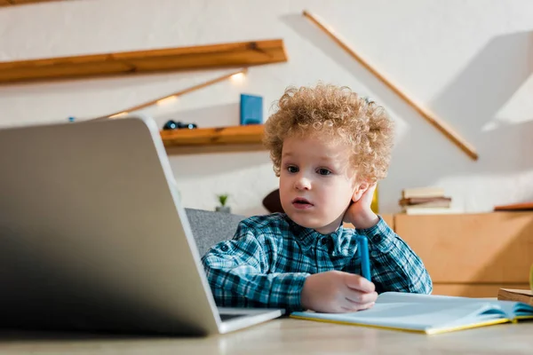 Enfoque selectivo del niño sosteniendo la pluma mientras estudia cerca de la computadora portátil en casa - foto de stock